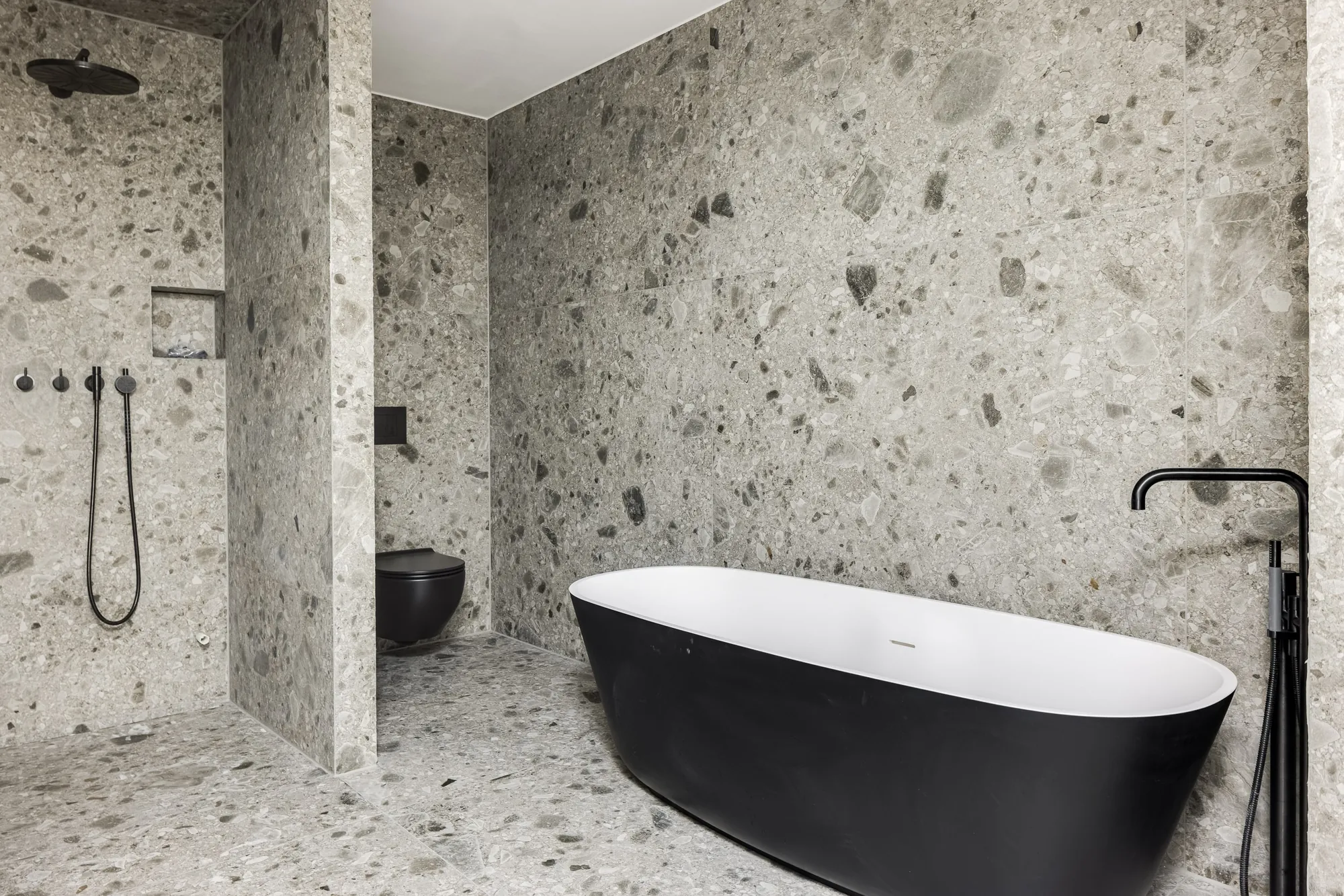 Bad mit Terrazzo-Fliesen und schwarzer freistehender Wanne