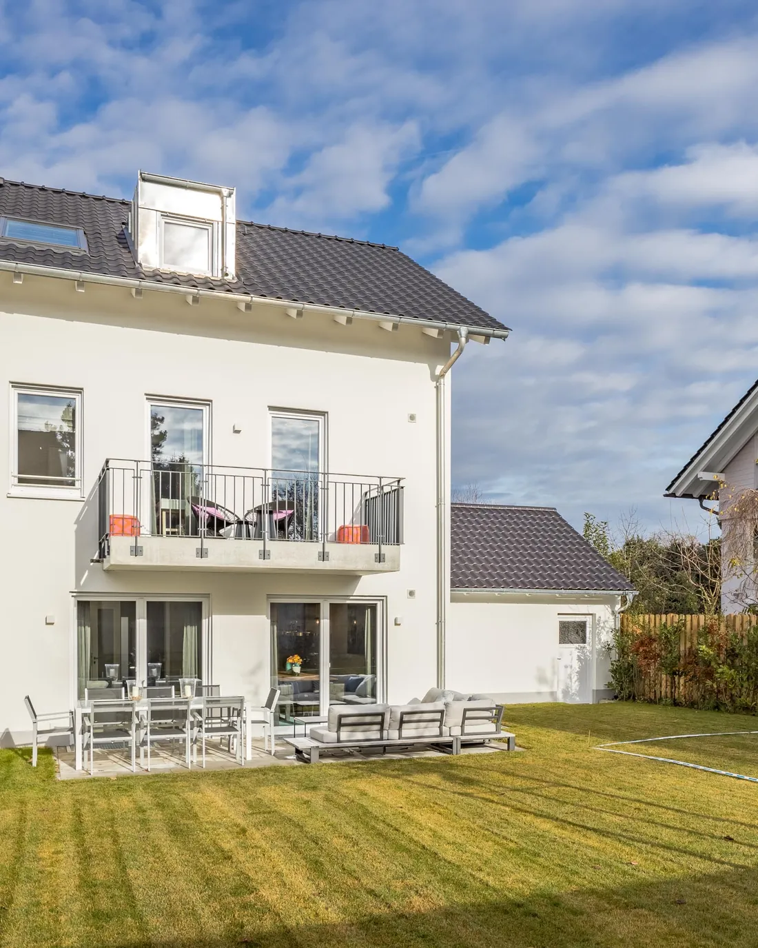 Weißes Doppelhaus mit Balkonen und jungem Baum im Garten
