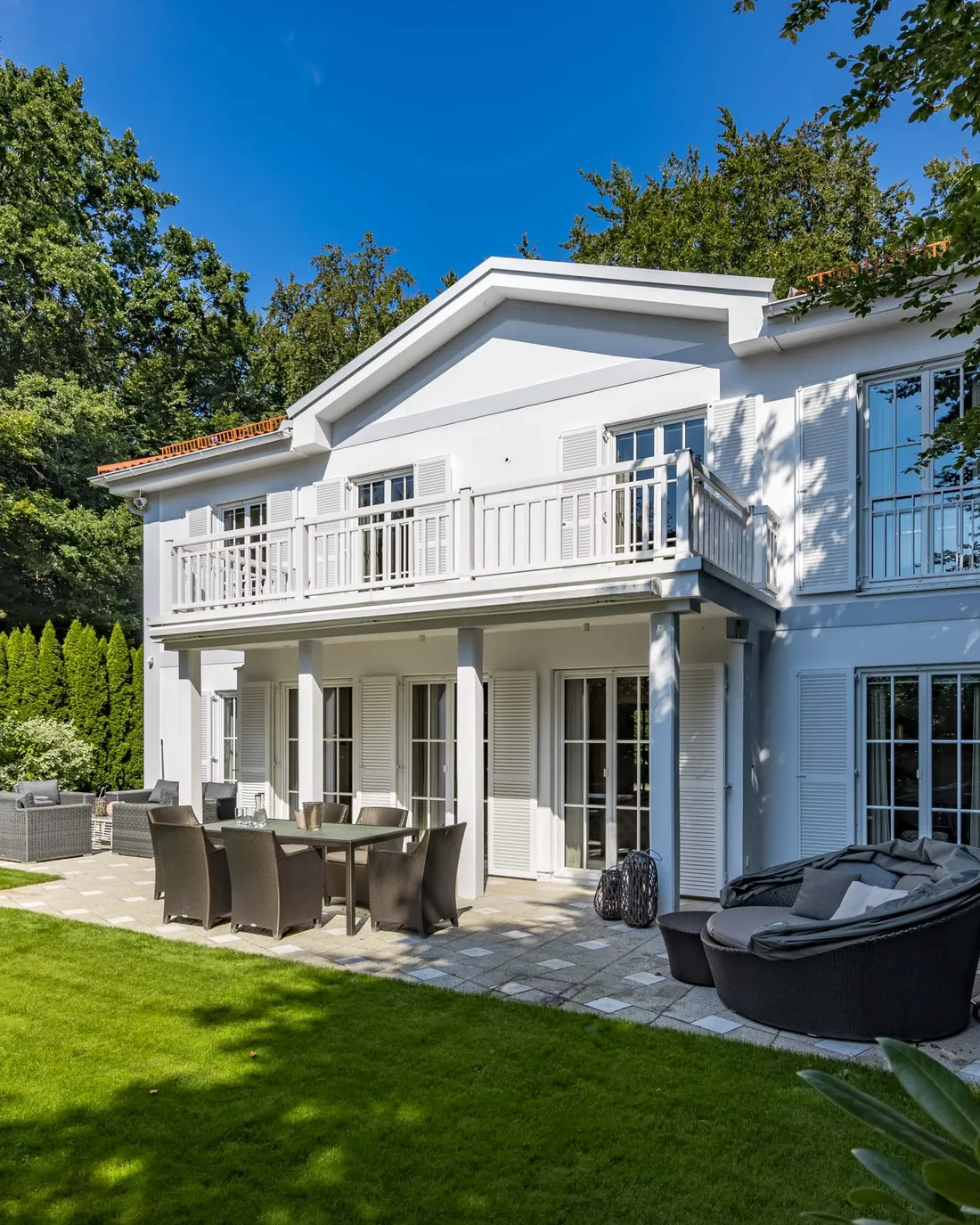 Klassische weiße Villa mit Terrasse vor hohen Bäumen